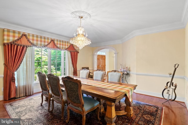 dining area with baseboards, arched walkways, ornamental molding, wood finished floors, and a notable chandelier