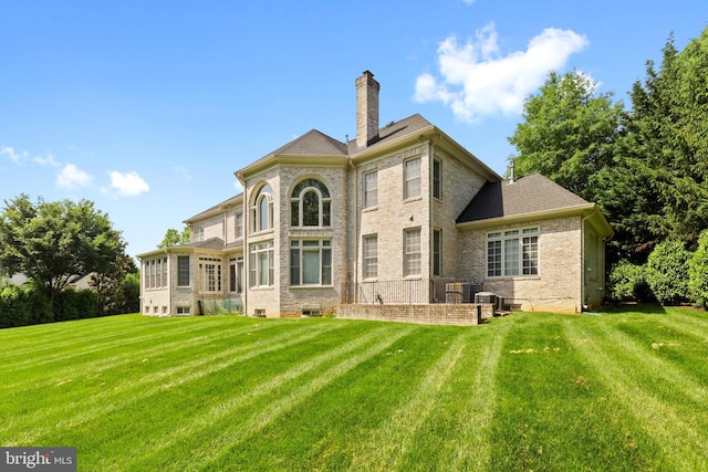 back of property featuring brick siding, a chimney, and a lawn