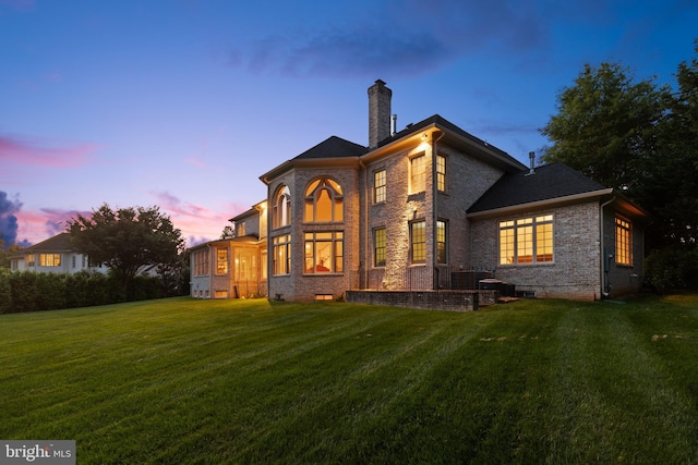 back of property featuring brick siding, crawl space, a chimney, and a lawn