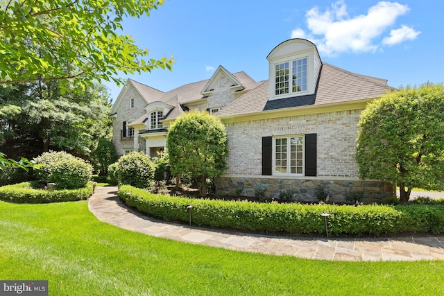 view of front facade with brick siding, stone siding, a front lawn, and roof with shingles