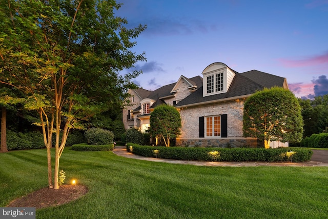 view of front of property featuring brick siding, a shingled roof, stone siding, and a yard