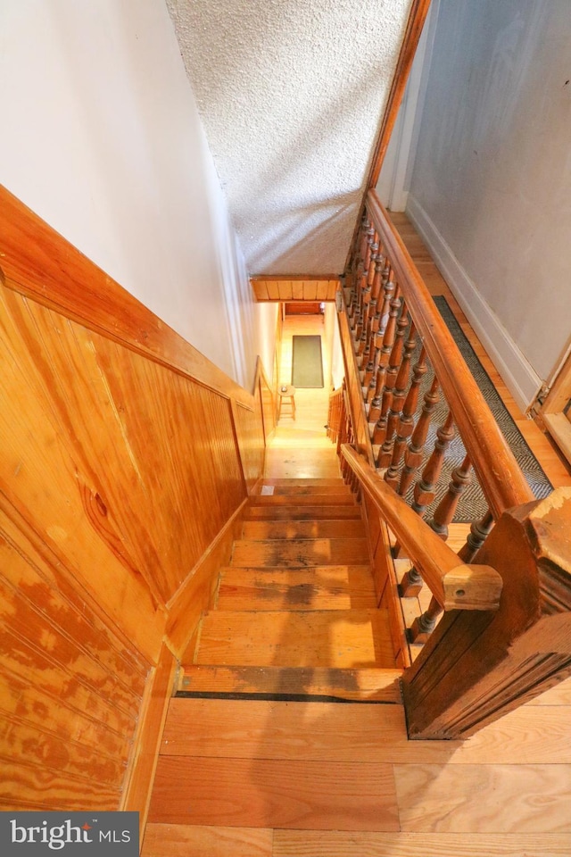 staircase with wooden walls, wood-type flooring, and a textured ceiling