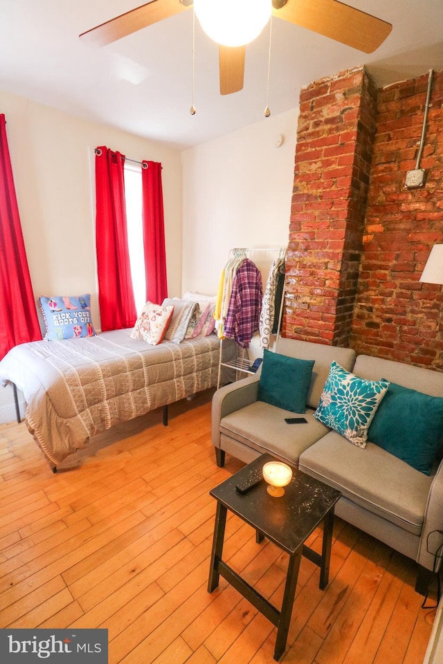 bedroom featuring ceiling fan, brick wall, and wood-type flooring