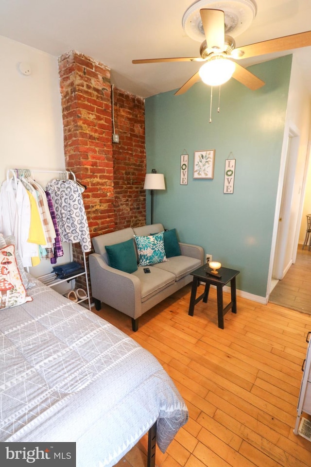 bedroom with baseboards, ceiling fan, light wood-style flooring, and brick wall