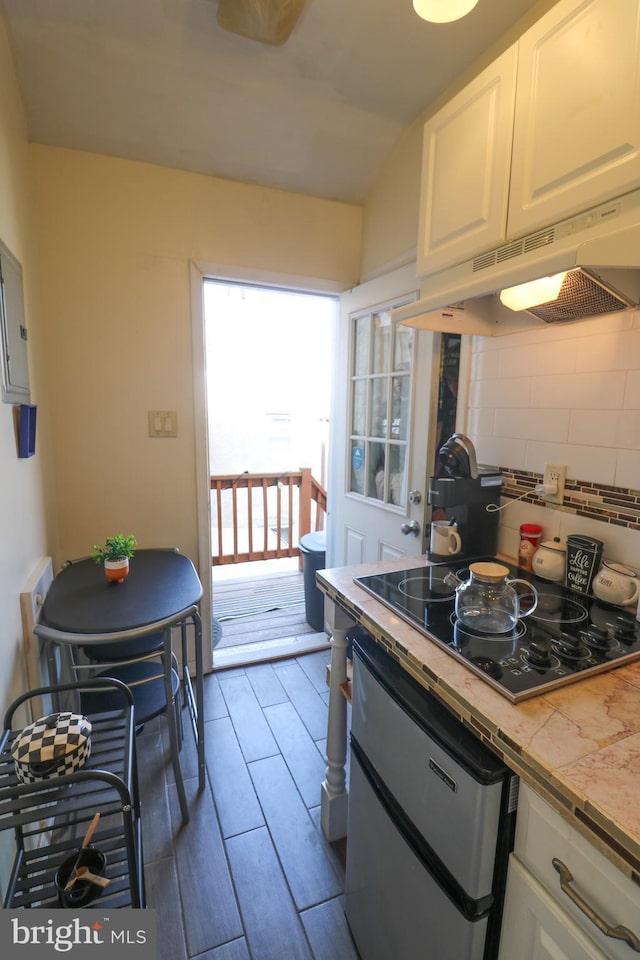 kitchen featuring black electric cooktop, under cabinet range hood, white cabinetry, wood tiled floor, and tasteful backsplash