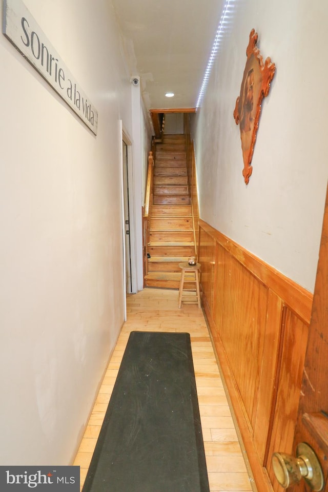 hallway with light wood-style floors, wainscoting, and stairs