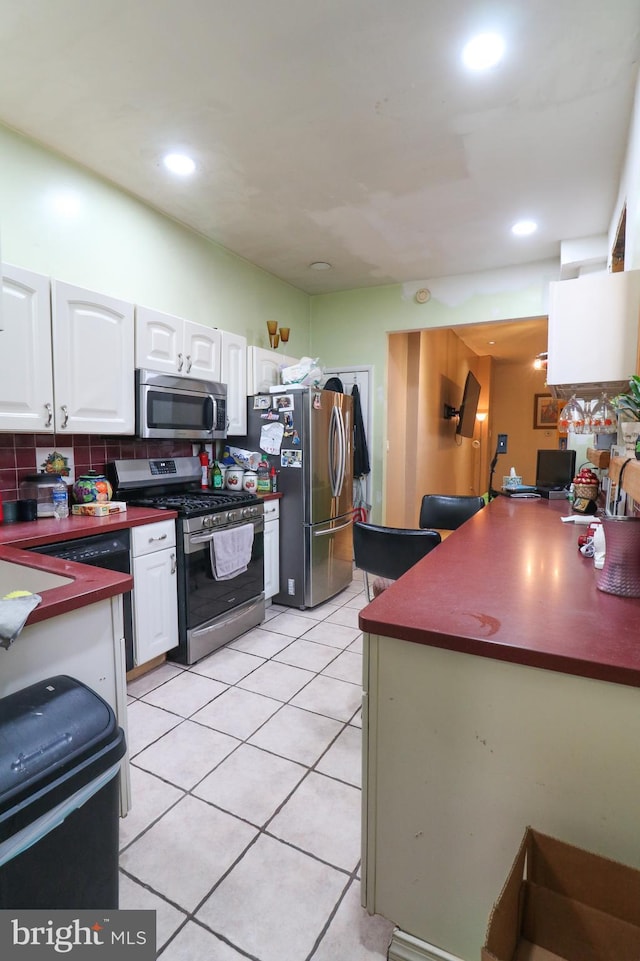 kitchen with light tile patterned floors, white cabinetry, appliances with stainless steel finishes, backsplash, and dark countertops