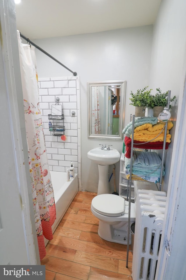 full bathroom featuring toilet, a sink, wood finished floors, radiator heating unit, and shower / bath combo