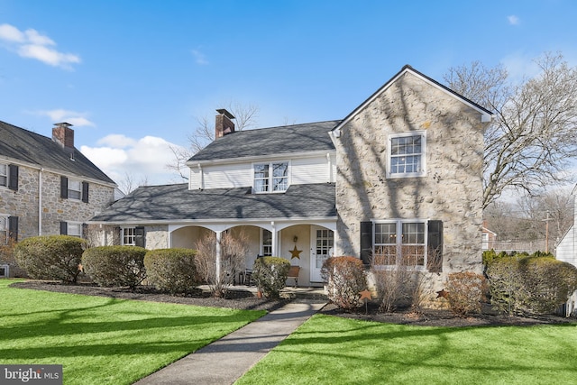 traditional-style house featuring a shingled roof, a chimney, a porch, and a front yard