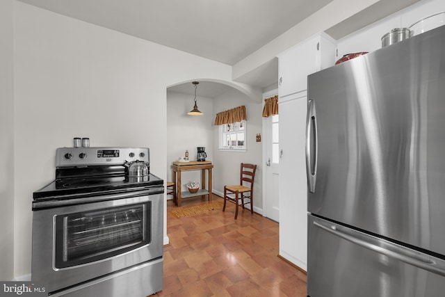 kitchen with arched walkways, pendant lighting, stainless steel appliances, white cabinetry, and baseboards