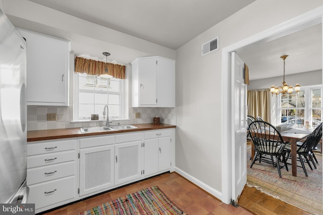 kitchen featuring a chandelier, a sink, visible vents, tasteful backsplash, and stainless steel fridge