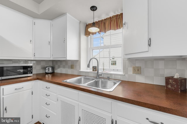 kitchen featuring white cabinets, dark countertops, stainless steel microwave, a sink, and backsplash