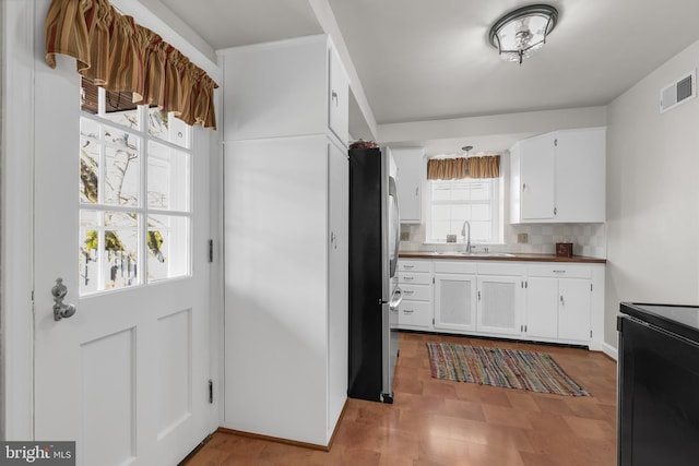 kitchen with freestanding refrigerator, visible vents, black range with electric cooktop, and white cabinetry