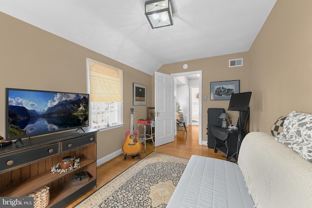 bedroom with lofted ceiling, wood finished floors, visible vents, and baseboards