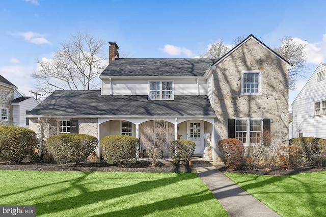 view of front of property featuring covered porch, roof with shingles, a chimney, and a front lawn