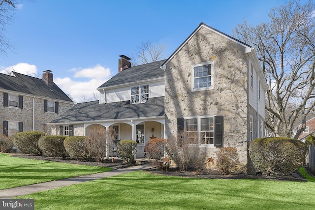 view of front facade with a shingled roof, covered porch, a front lawn, and stucco siding