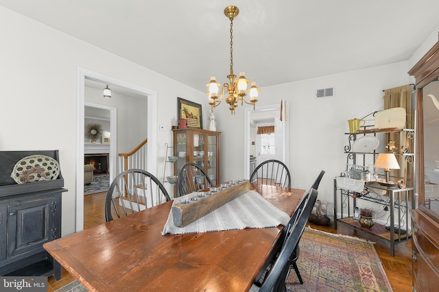 dining area featuring a warm lit fireplace, wood finished floors, a chandelier, and visible vents