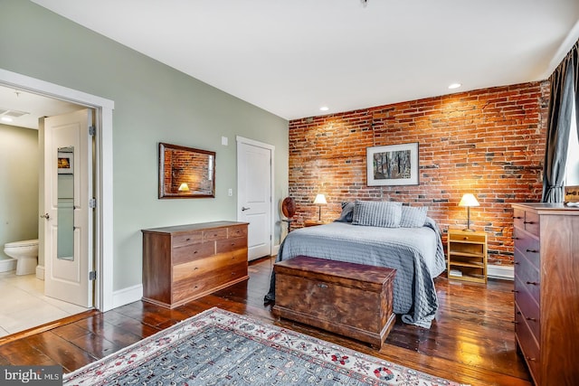 bedroom featuring brick wall, hardwood / wood-style floors, connected bathroom, and baseboards