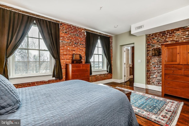 bedroom with baseboards, visible vents, brick wall, and wood finished floors