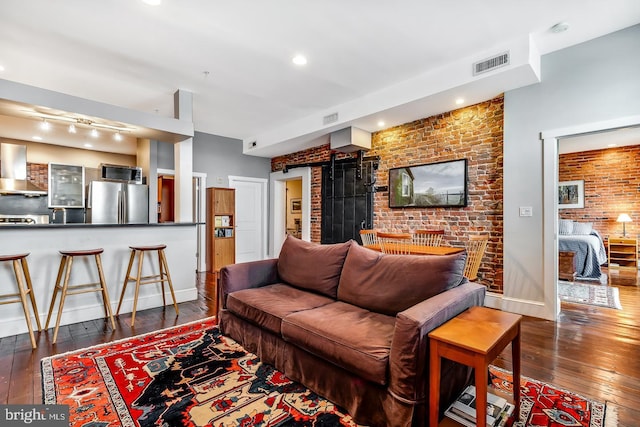 living area featuring baseboards, brick wall, visible vents, and dark wood-type flooring