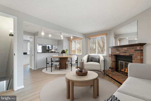 living area featuring light wood-type flooring, a fireplace, a textured ceiling, and baseboards