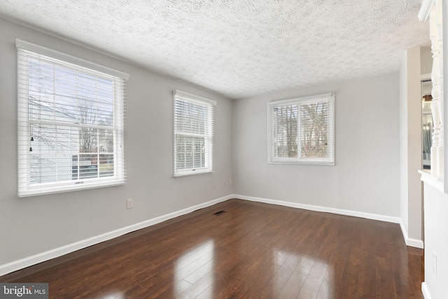 empty room featuring baseboards, a textured ceiling, hardwood / wood-style flooring, and a healthy amount of sunlight