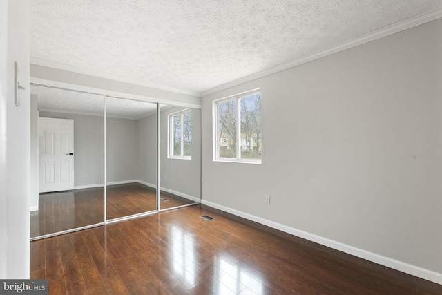 unfurnished bedroom featuring crown molding, visible vents, a textured ceiling, wood finished floors, and baseboards