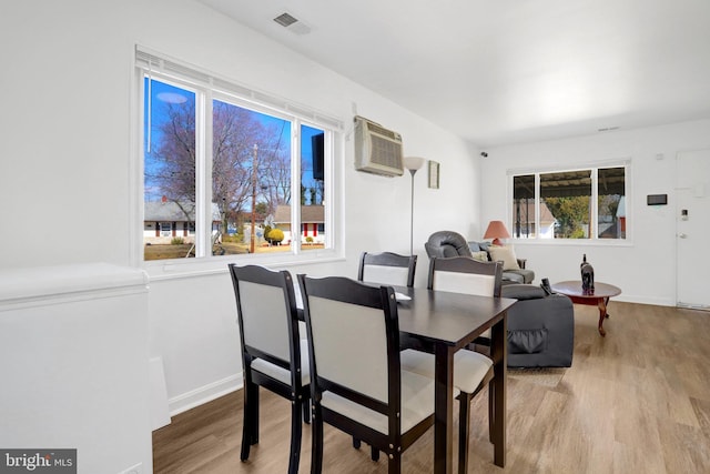 dining room featuring visible vents, a wall mounted AC, baseboards, and wood finished floors