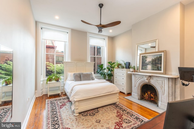 bedroom featuring recessed lighting, a fireplace with flush hearth, a ceiling fan, baseboards, and light wood finished floors