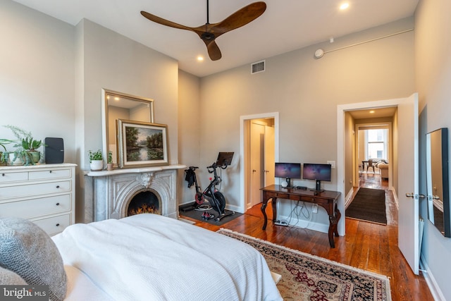 bedroom featuring a warm lit fireplace, recessed lighting, wood finished floors, visible vents, and baseboards