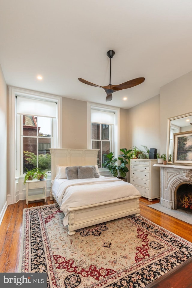 bedroom featuring ceiling fan, light wood-type flooring, a fireplace with flush hearth, and recessed lighting