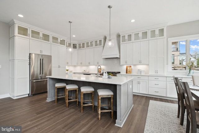 kitchen featuring an island with sink, high quality fridge, glass insert cabinets, and light countertops