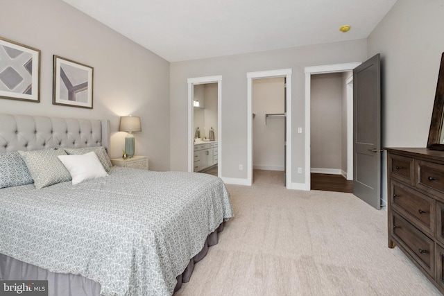 bedroom with light carpet, baseboards, connected bathroom, a walk in closet, and a closet