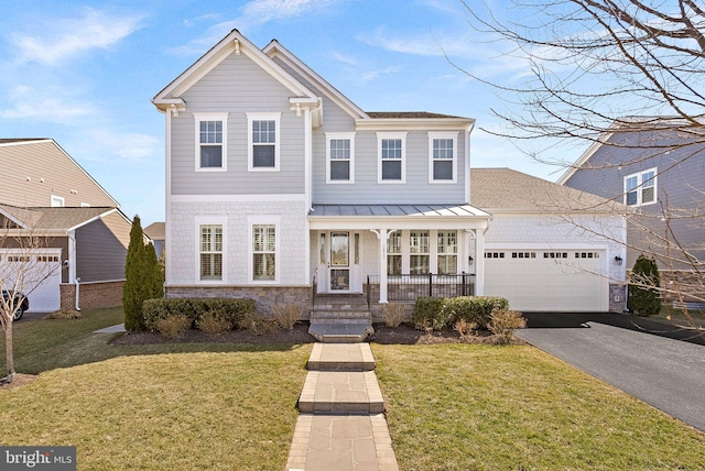 traditional home with a porch, aphalt driveway, an attached garage, a standing seam roof, and a front lawn