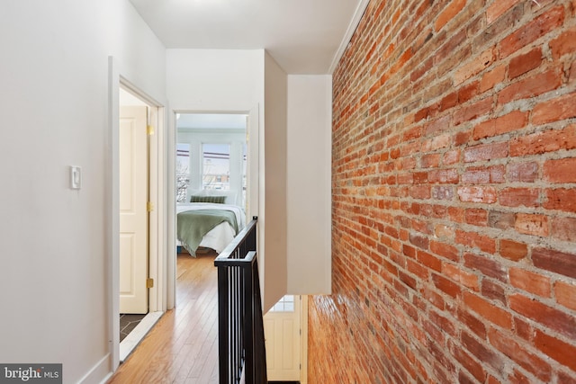 hall with an accent wall, light wood finished floors, and brick wall