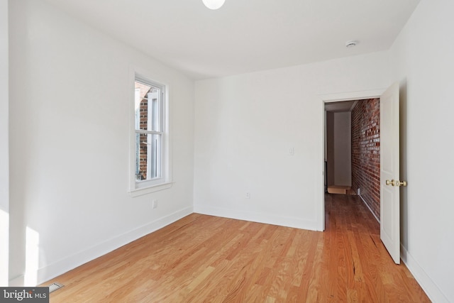 unfurnished room with light wood-style floors, brick wall, and baseboards