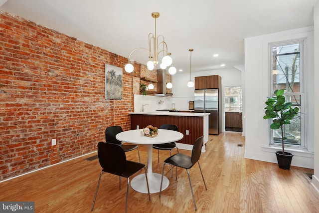 dining space featuring a chandelier, brick wall, recessed lighting, and light wood-style floors