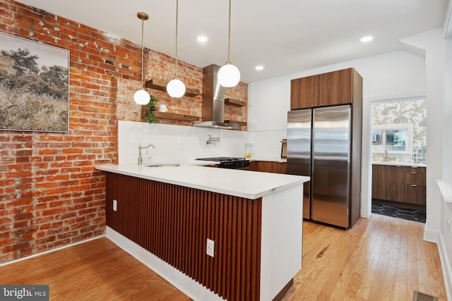 kitchen featuring a peninsula, wall chimney range hood, light countertops, and freestanding refrigerator