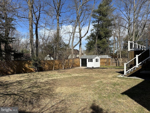 view of yard featuring an outbuilding, a storage unit, a fenced backyard, and stairs