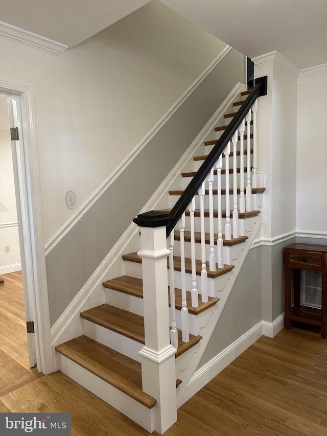 staircase with ornamental molding, baseboards, and wood finished floors