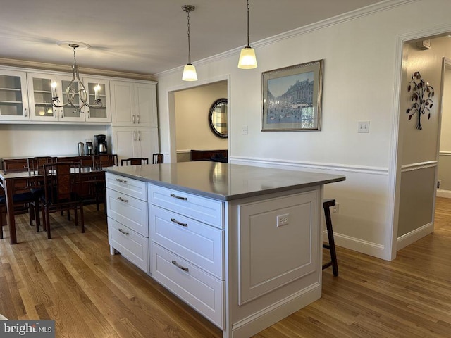 kitchen with wood finished floors, a kitchen island, white cabinetry, glass insert cabinets, and pendant lighting