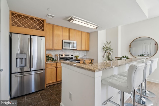 kitchen with a breakfast bar area, light stone counters, visible vents, decorative backsplash, and appliances with stainless steel finishes