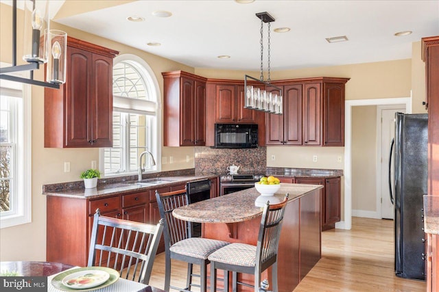 kitchen featuring a kitchen island, a breakfast bar, light wood-type flooring, black appliances, and a sink