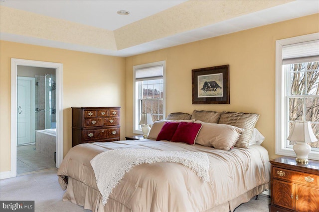 bedroom featuring light carpet, ensuite bathroom, and a tray ceiling