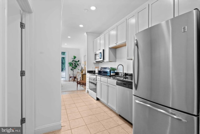 kitchen featuring light tile patterned floors, dark countertops, stainless steel appliances, a sink, and recessed lighting