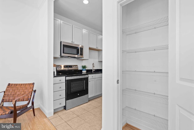 kitchen with light tile patterned floors, baseboards, dark countertops, stainless steel appliances, and a sink