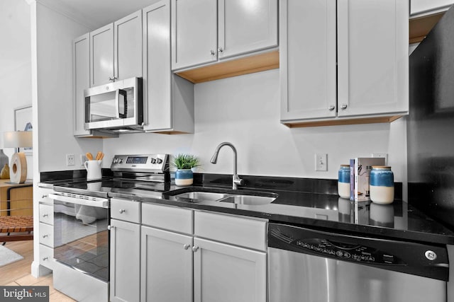 kitchen featuring appliances with stainless steel finishes, dark stone counters, a sink, and light wood finished floors