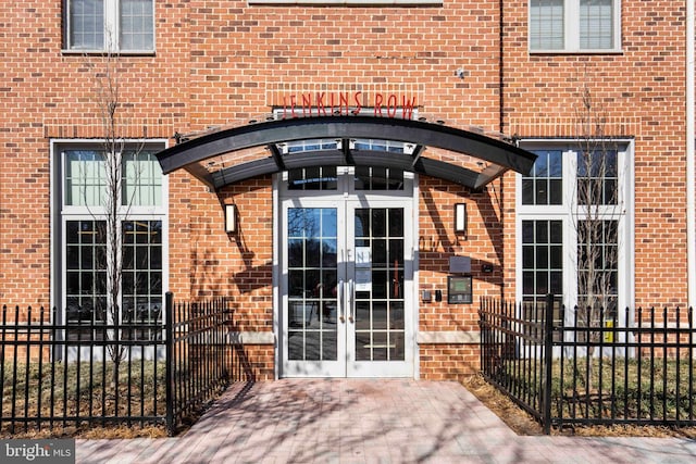 view of exterior entry with french doors, fence, and brick siding