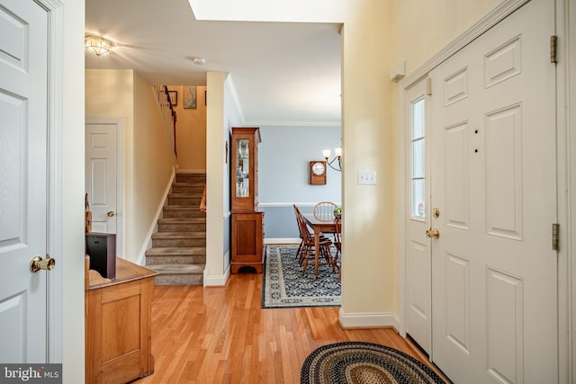 entrance foyer with baseboards, stairs, crown molding, light wood-style floors, and a notable chandelier