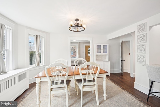 dining area with radiator, dark wood-style floors, baseboards, and a notable chandelier